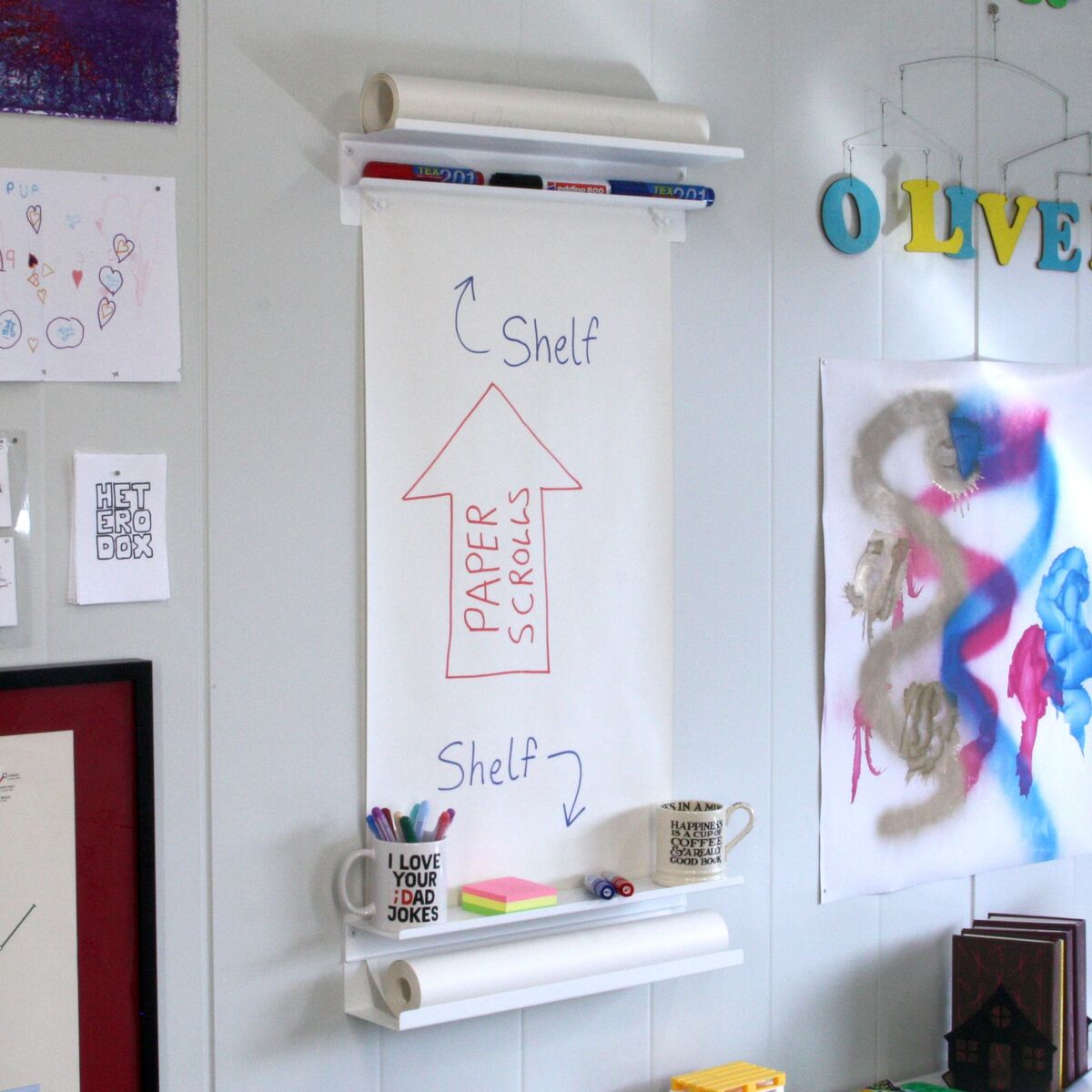 VÄGGRULLE mounted on a wall, with a hand-drawn diagram on the paper showing the shelves and the upward-feeding paper scroll
